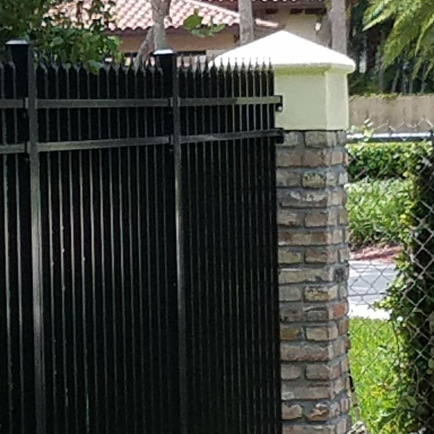 A black fence with a white brick post in front of a house.
