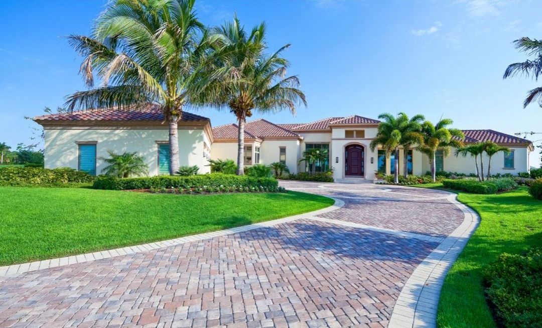 A large white house with a brick driveway and palm trees in front of it.
