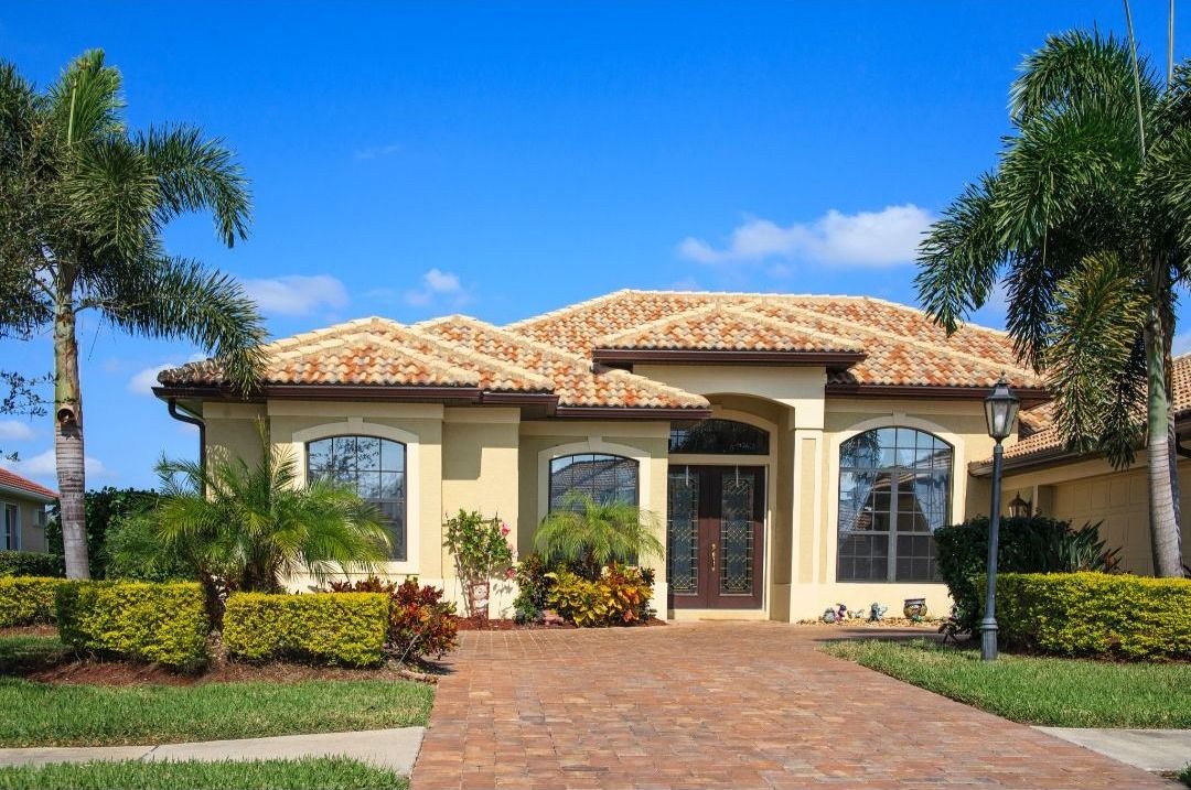 A large house with a brick driveway and palm trees in front of it.