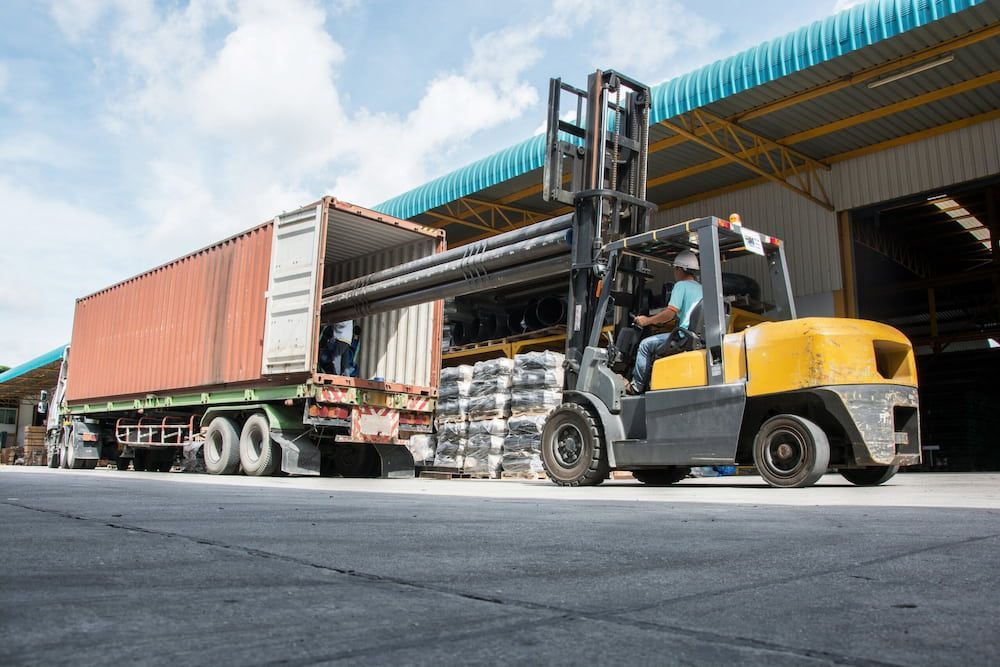 A Forklift Is Loading A Container Onto A Truck In A Warehouse — Newcastle Moving & Storage in Salt Ash, NSW