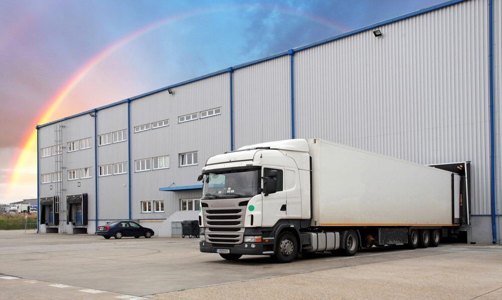 A White Semi Truck Is Parked In Front Of A Large Warehouse — Newcastle Moving & Storage in Salt Ash, NSW