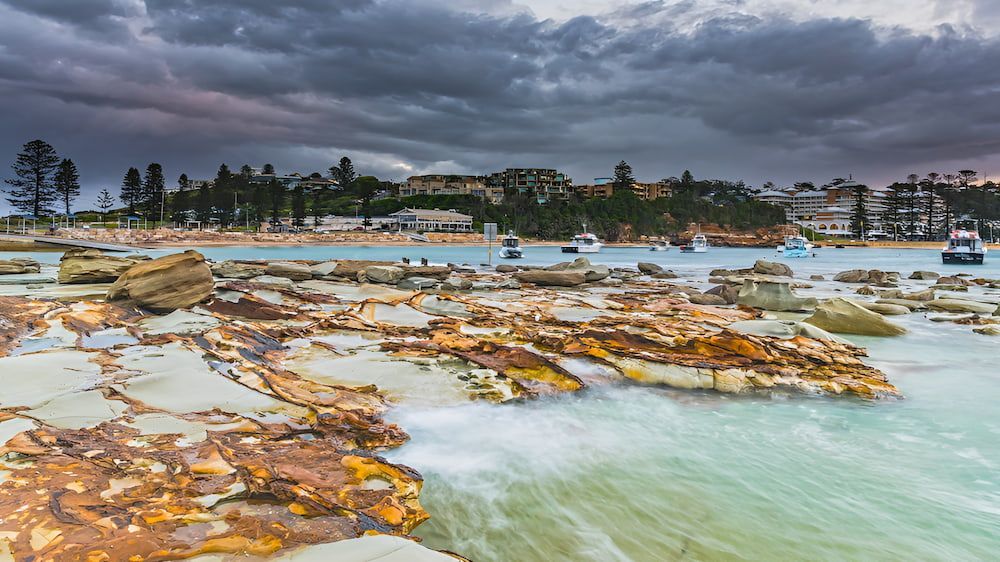 A Beach With Rocks And Boats In The Water On A Cloudy Day — Newcastle Moving & Storage in Gosford, NSW