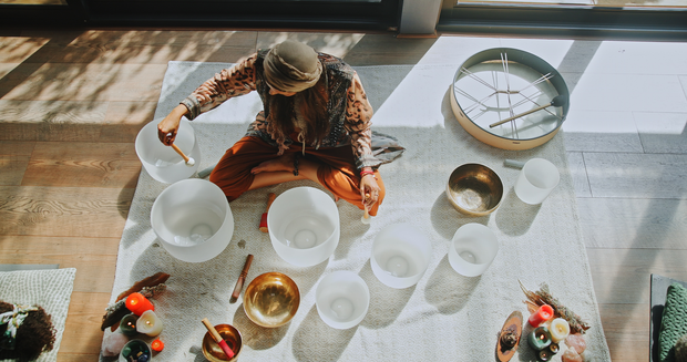 Person playing crystal singing bowls on a rug in a sunlit room.