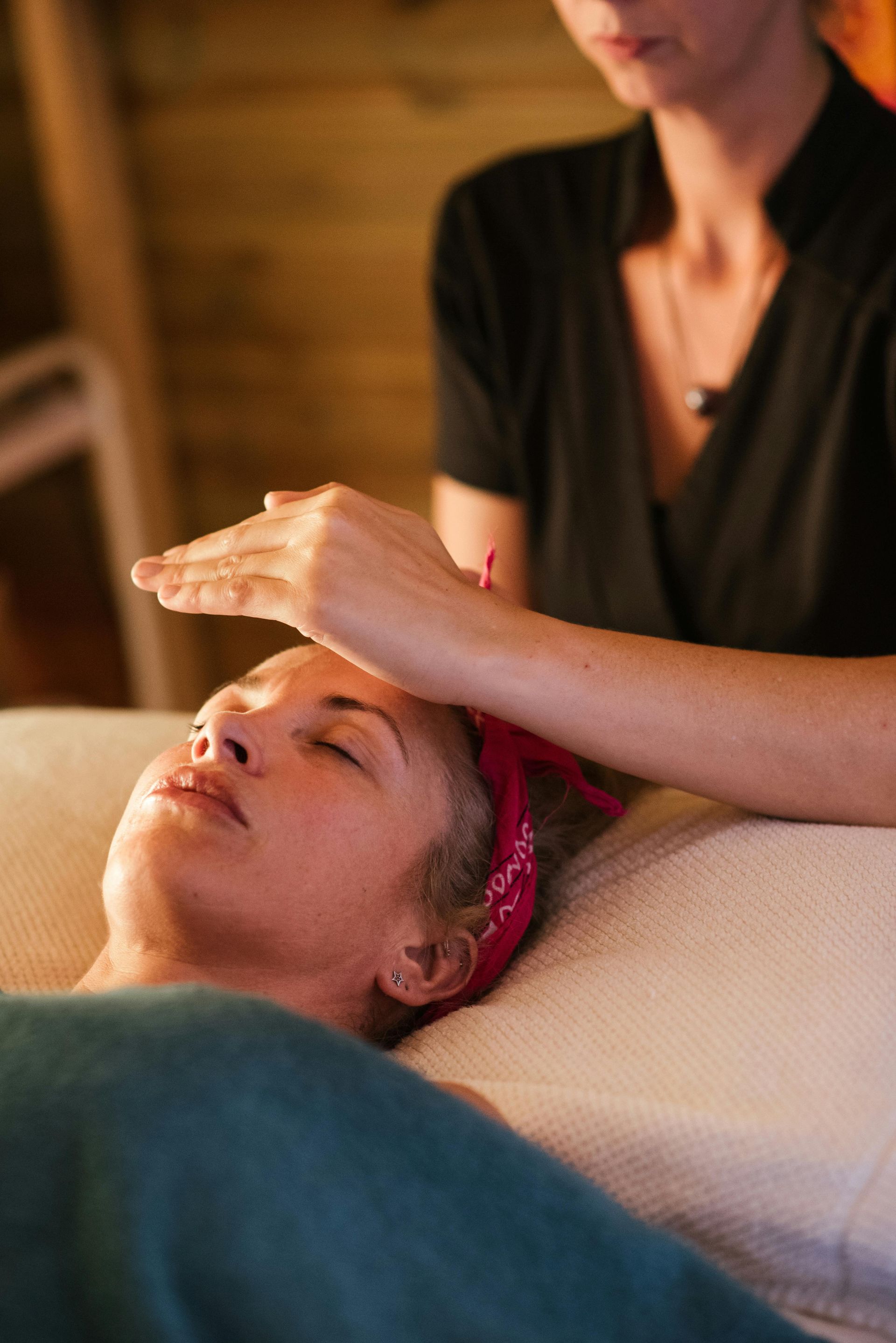 Woman receiving reiki treatment; therapist's hands over her forehead. Eyes closed. Indoor setting.