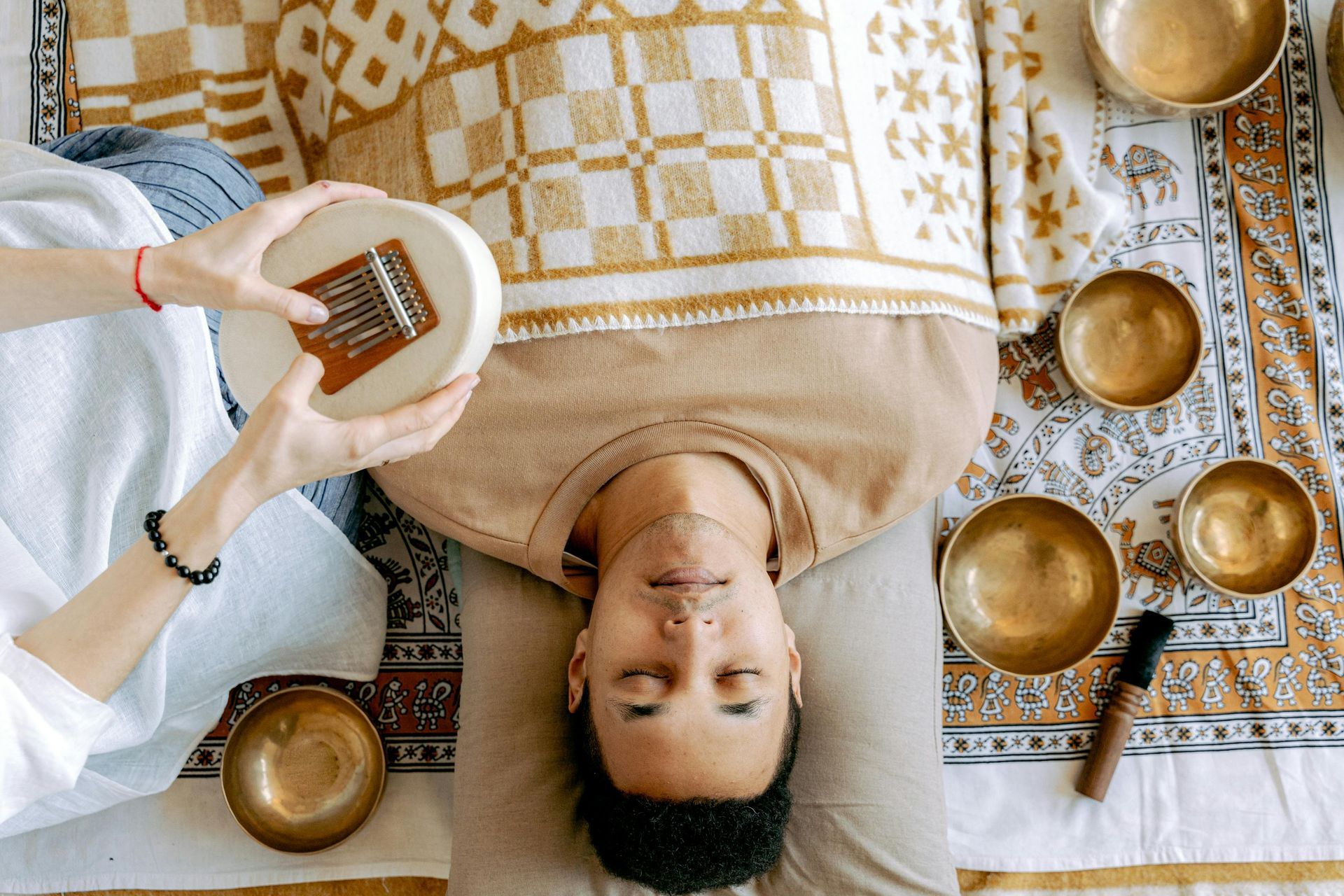 Person receiving sound healing with bowls, a kalimba, and a patterned cloth.
