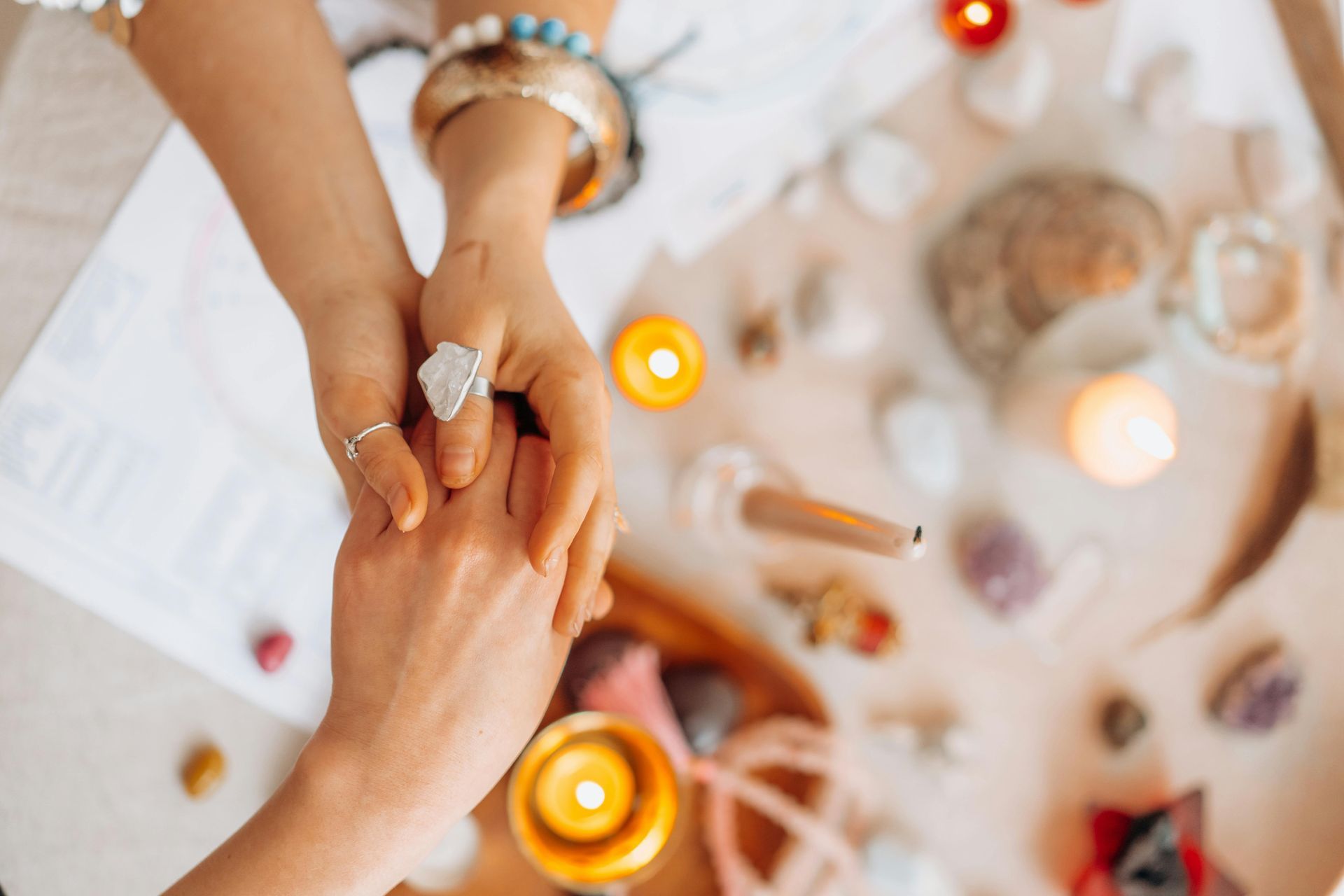 Two hands holding, surrounded by candles, crystals, and spiritual objects.