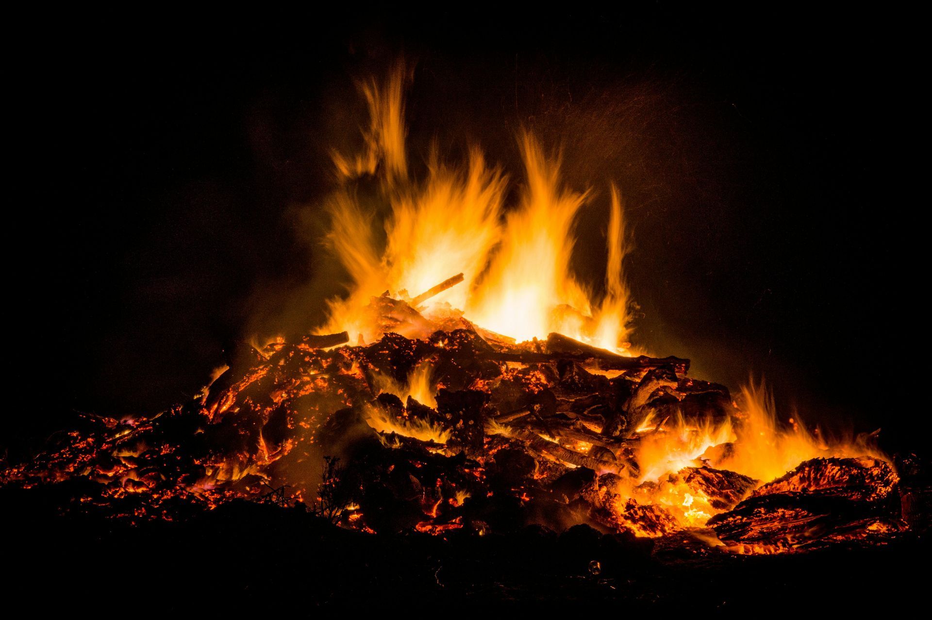 Glowing bonfire at night, flames reaching high above burning logs.