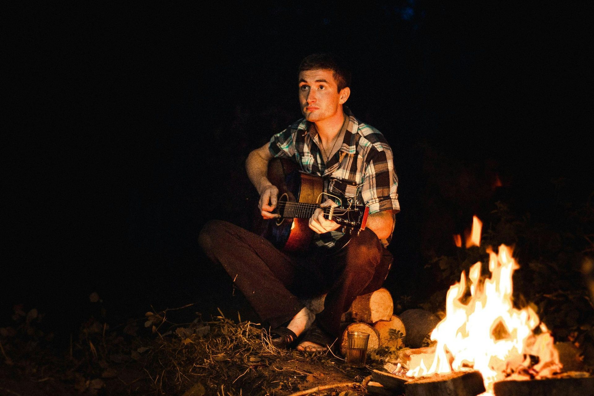 Man sitting by campfire playing guitar at night.