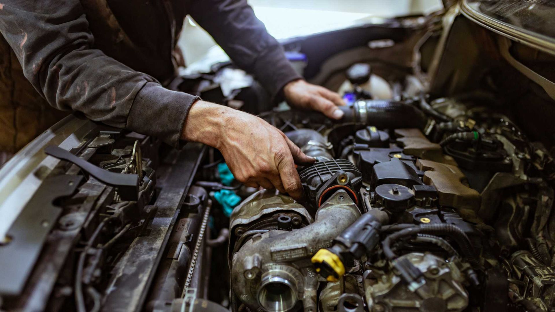Mechanic's hands working on a car engine in a garage.