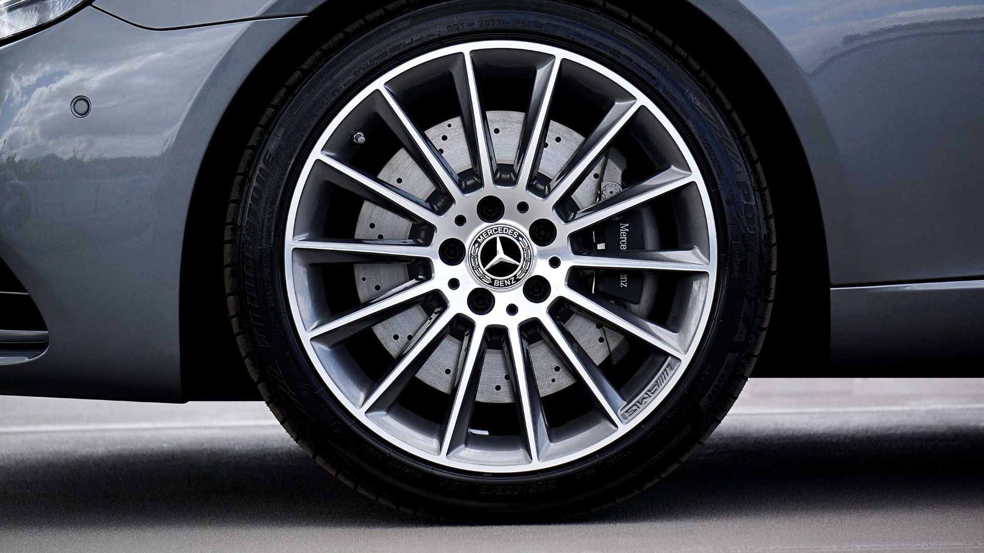 Mercedes-Benz car wheel; silver rim, black tire. The vehicle is gray; close-up, outdoors.