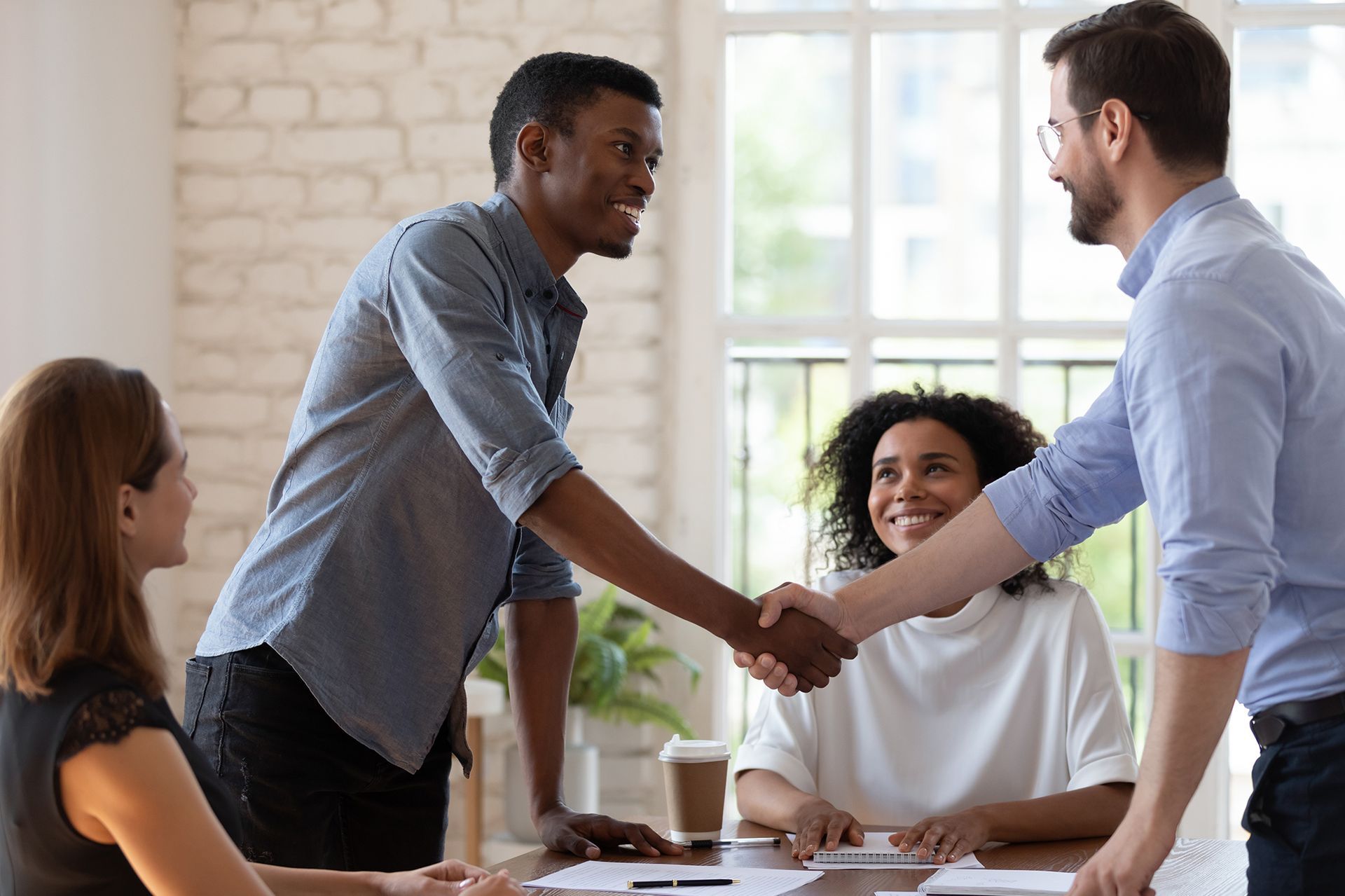 A group of people are shaking hands while sitting at a table.