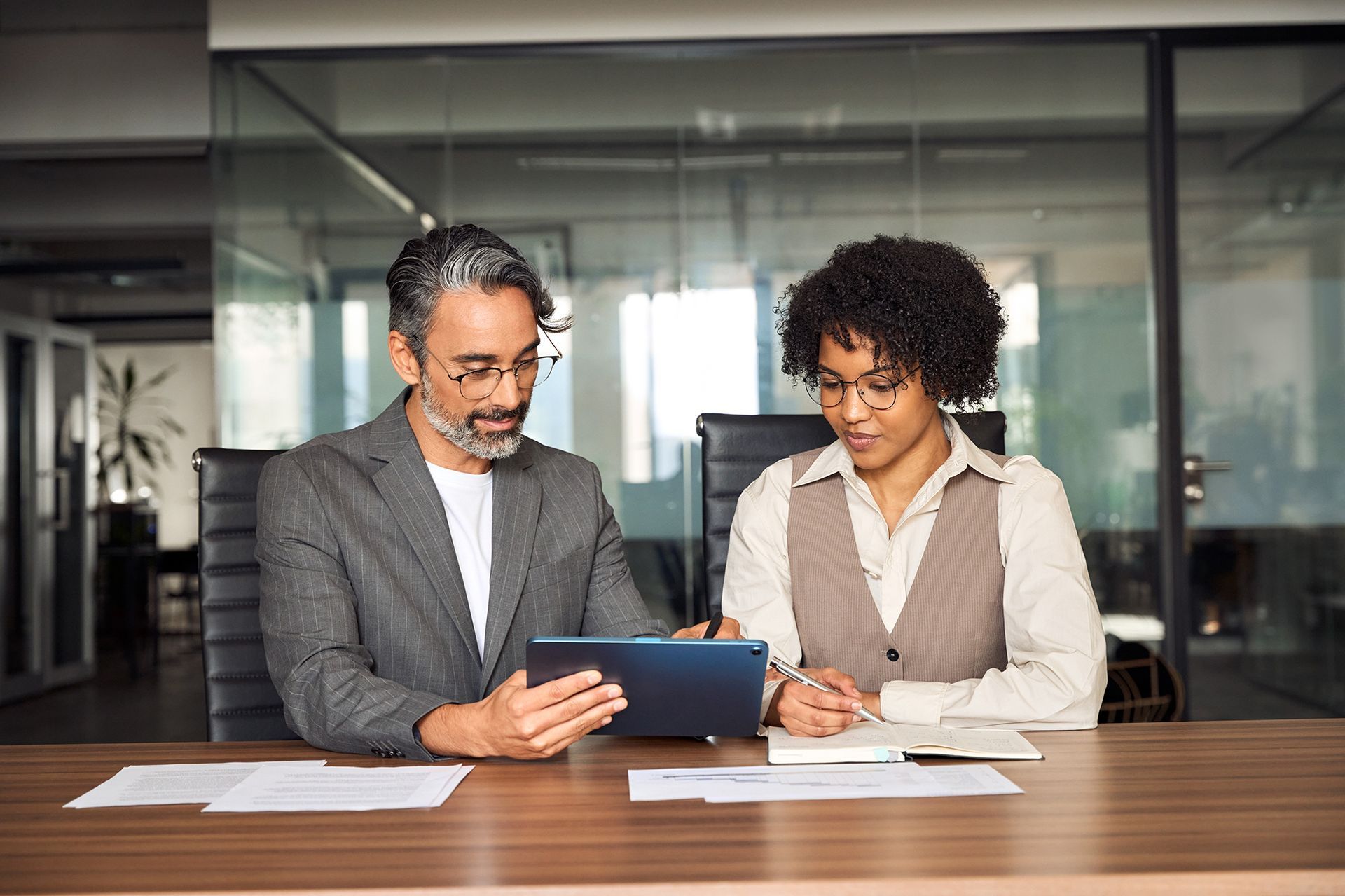 A man and a woman are sitting at a table looking at a tablet.