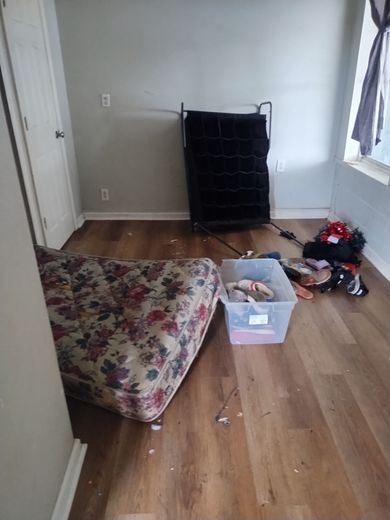 Room with mattress on floor, clothing, and wire frame furniture.