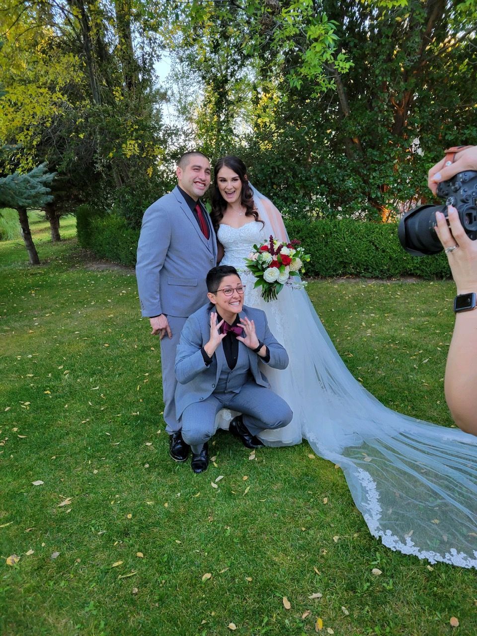 Wedding photo: Couple with photographer. Bride in white dress, groom in suit, third person squats.