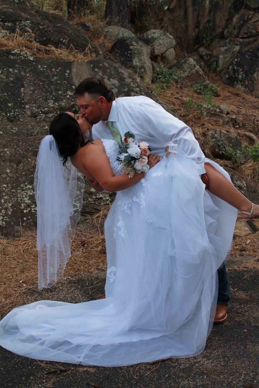Newlyweds embrace and kiss, with the groom lifting the bride in a mountain setting.