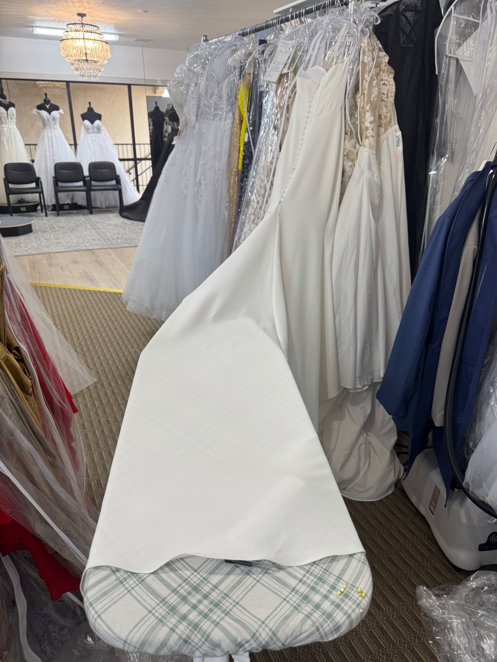 An ironing board with white fabric in a bridal shop, surrounded by gowns on racks.