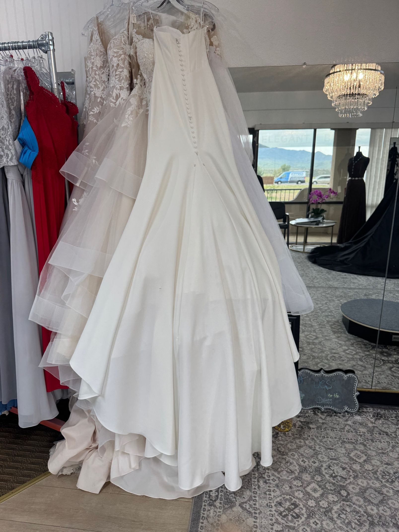 White wedding dress on display in a bridal shop, other dresses and a mirror in the background.