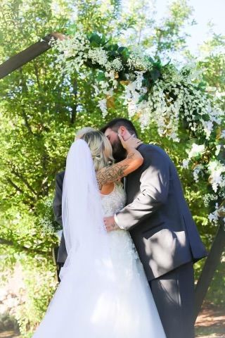 Couple kissing under floral arch during outdoor wedding.
