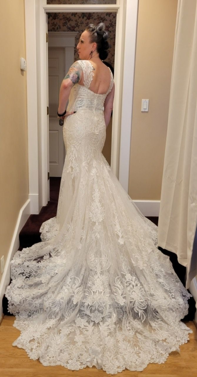 Woman in ornate white lace wedding dress, back to camera, standing in doorway. Long train.