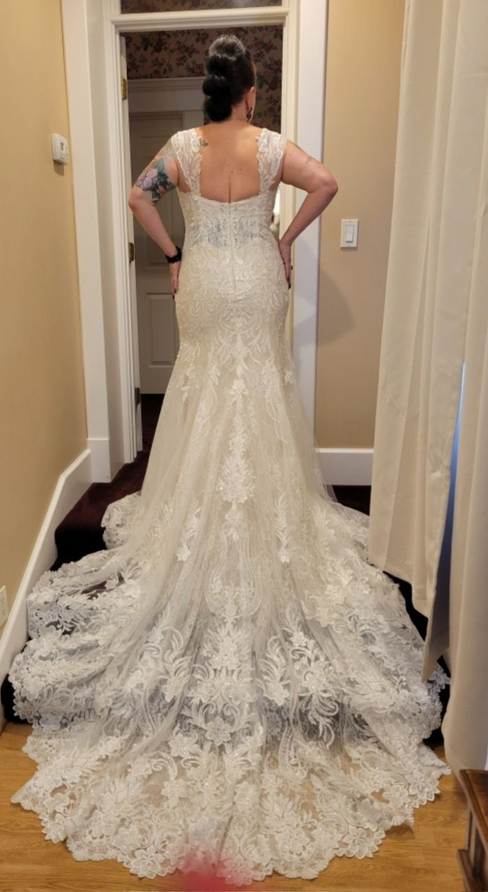 Woman in a white lace wedding dress, back view, standing in a hallway.