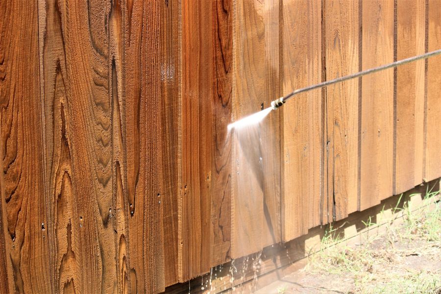 A person is using a high pressure washer to clean a wooden fence.