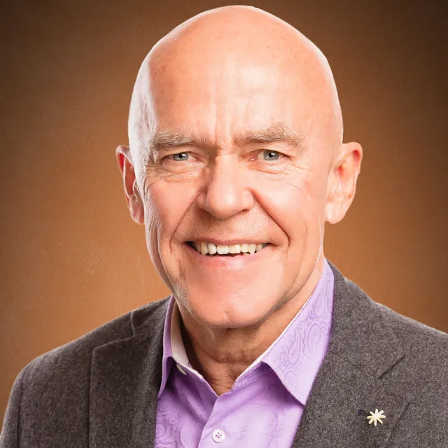 A bald man wearing a purple shirt and a grey jacket is smiling for the camera.