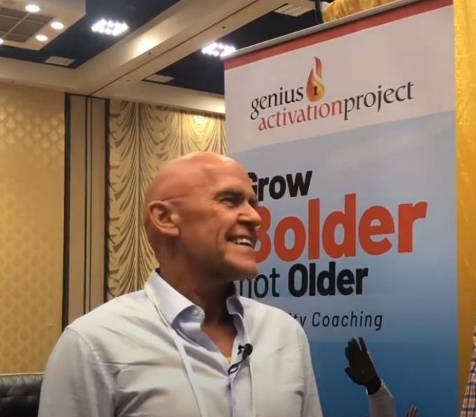 Bald man wearing a blue button-down shirt smiles at the camera. White backdrop.