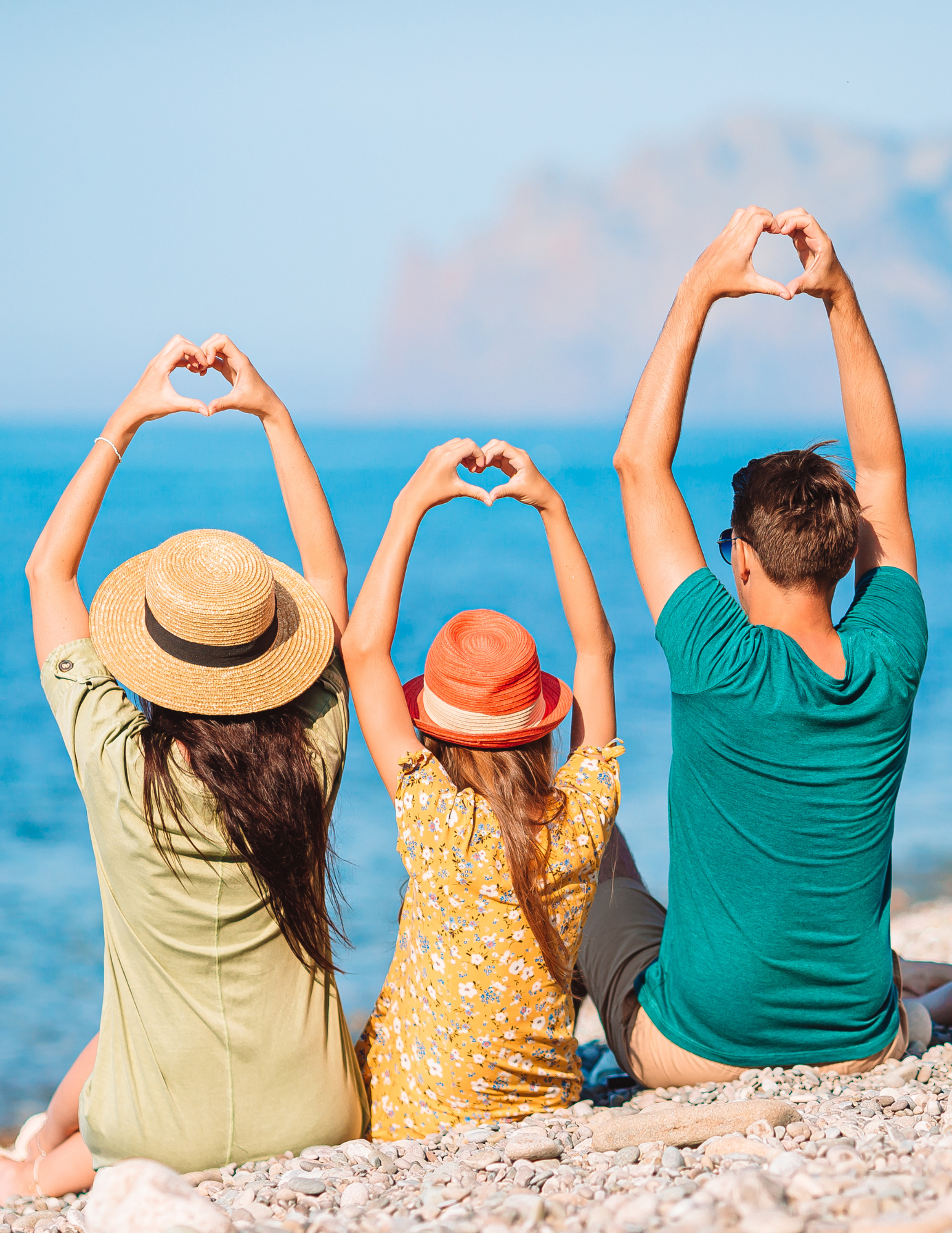 A family is sitting on the beach making a heart shape with their hands.