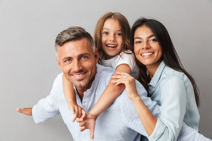 A man and woman are giving a little girl a piggyback ride.