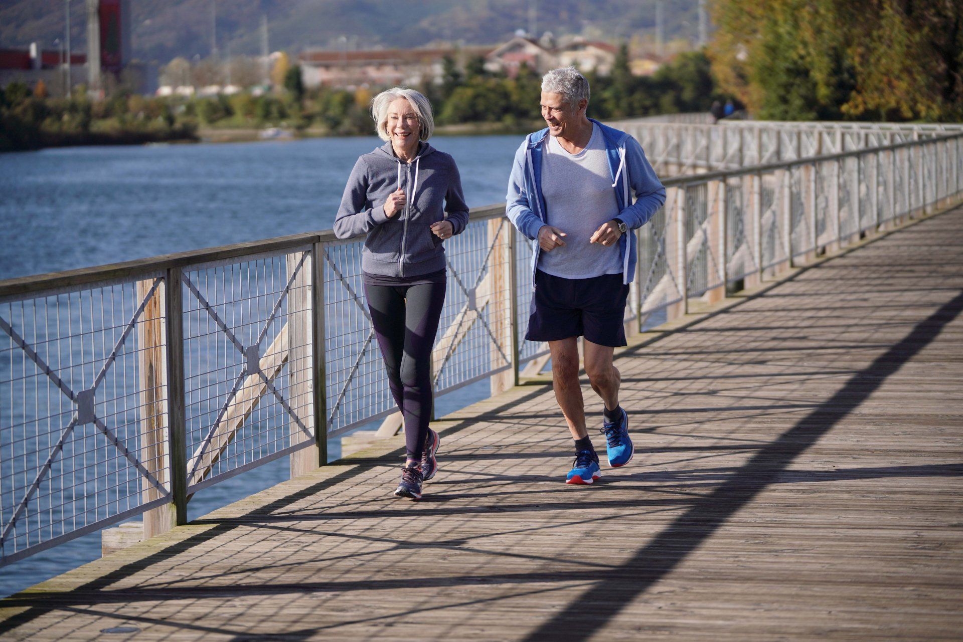 A man and a woman are jogging on a wooden bridge.