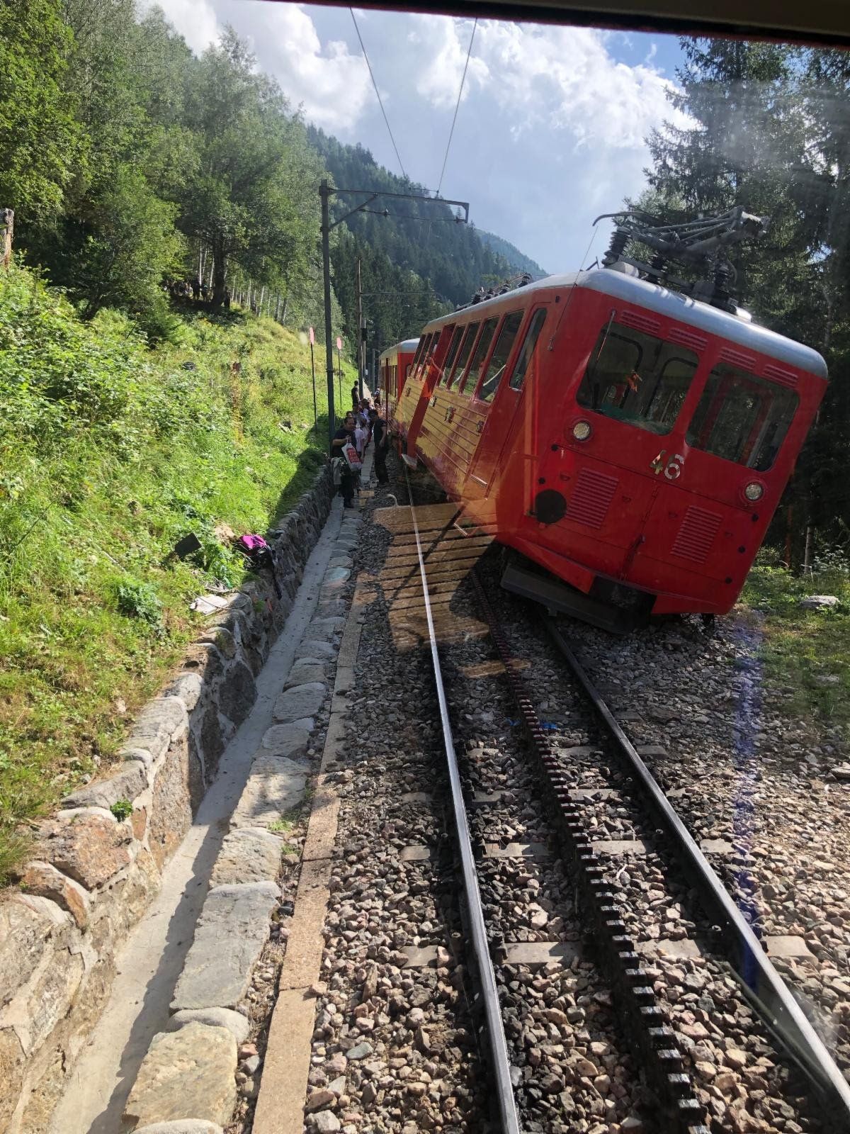 A red train is going down the tracks in the mountains