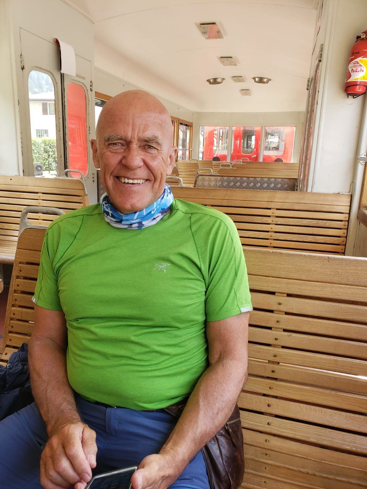 A man in a green shirt is sitting on a wooden bench and smiling.