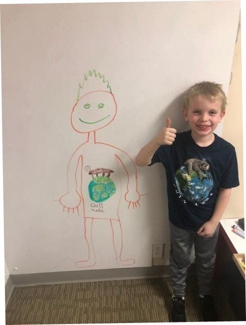 A young boy giving a thumbs up in front of a drawing of a man