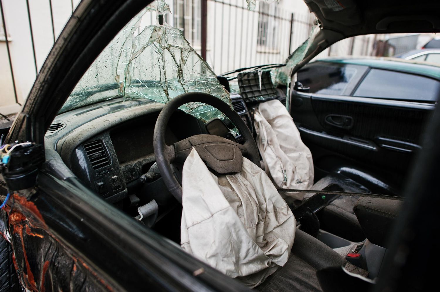 Interior of a severely damaged black car; deployed airbags, shattered windshield, and damaged dashboard.