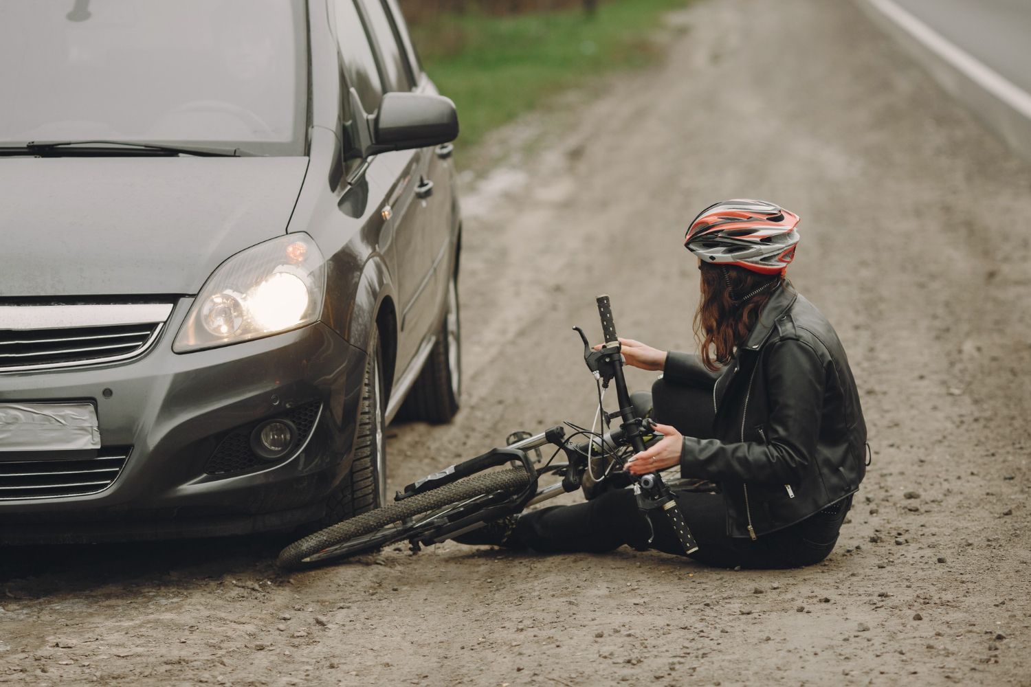 Car and cyclist: Cyclist sits on the ground with their bike beside a car on a road.