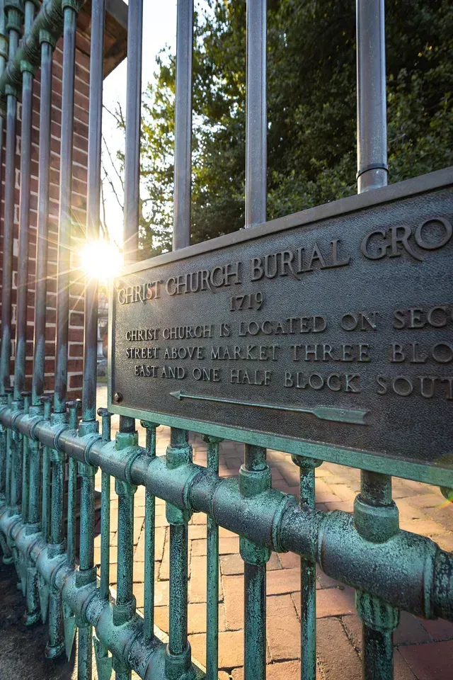 Gate to Christ Church Burial Ground with plaque, brick wall, and sunlight.