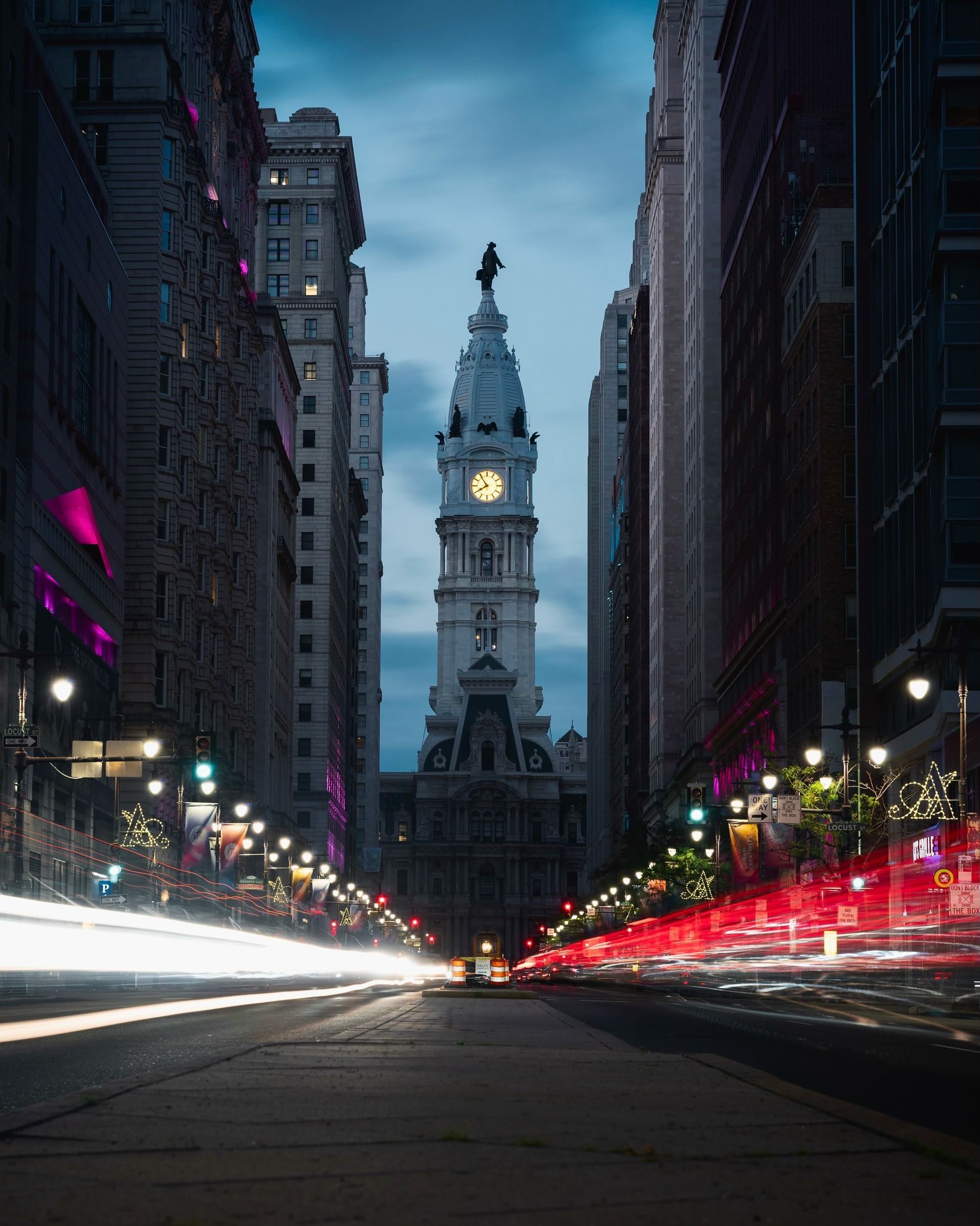 Philadelphia City Hall framed by a street lined with buildings and streaking car lights.