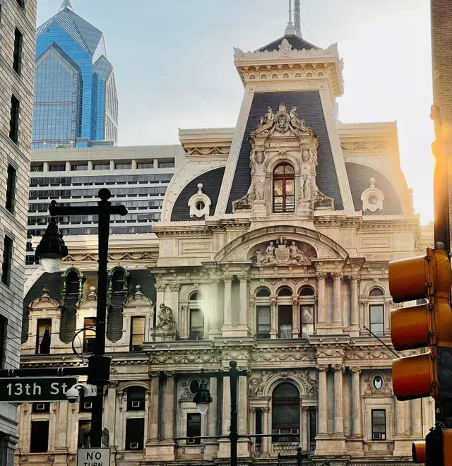 Philadelphia City Hall exterior with traffic light, 13th St sign, and modern skyscraper background.