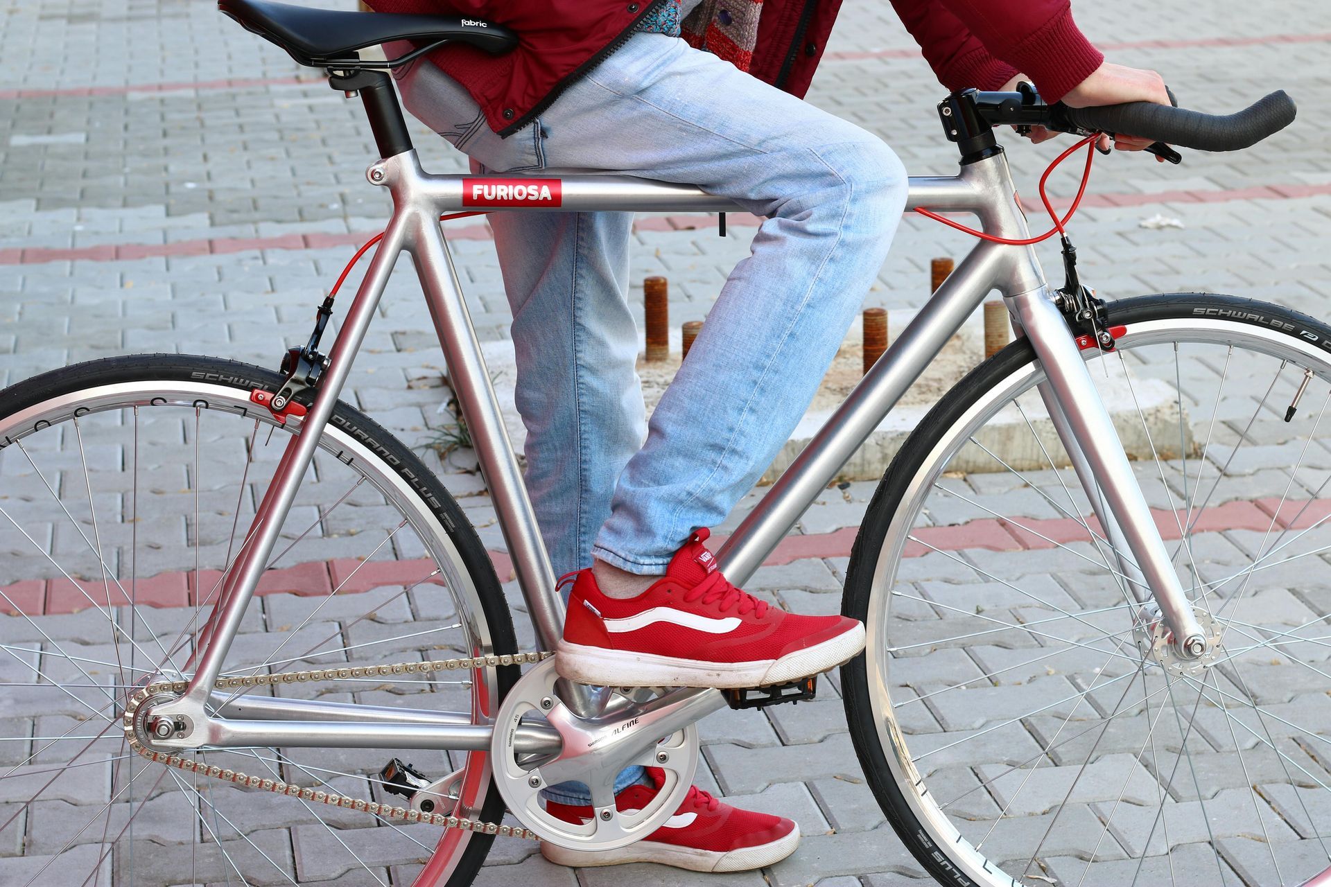 Person on a silver bicycle with red accents, wearing red shoes and blue jeans, outside.