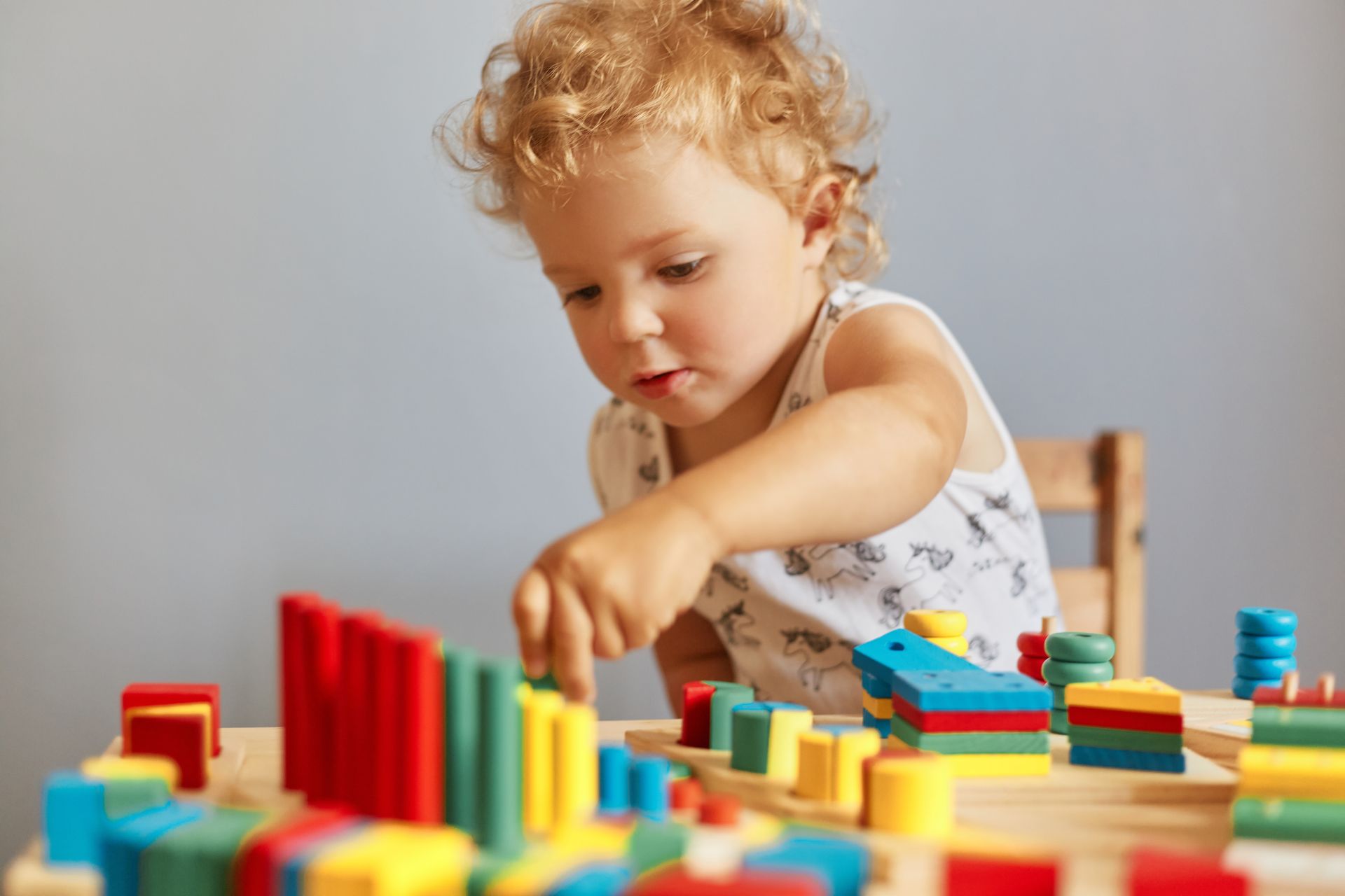 A little girl is playing with wooden blocks at a table.