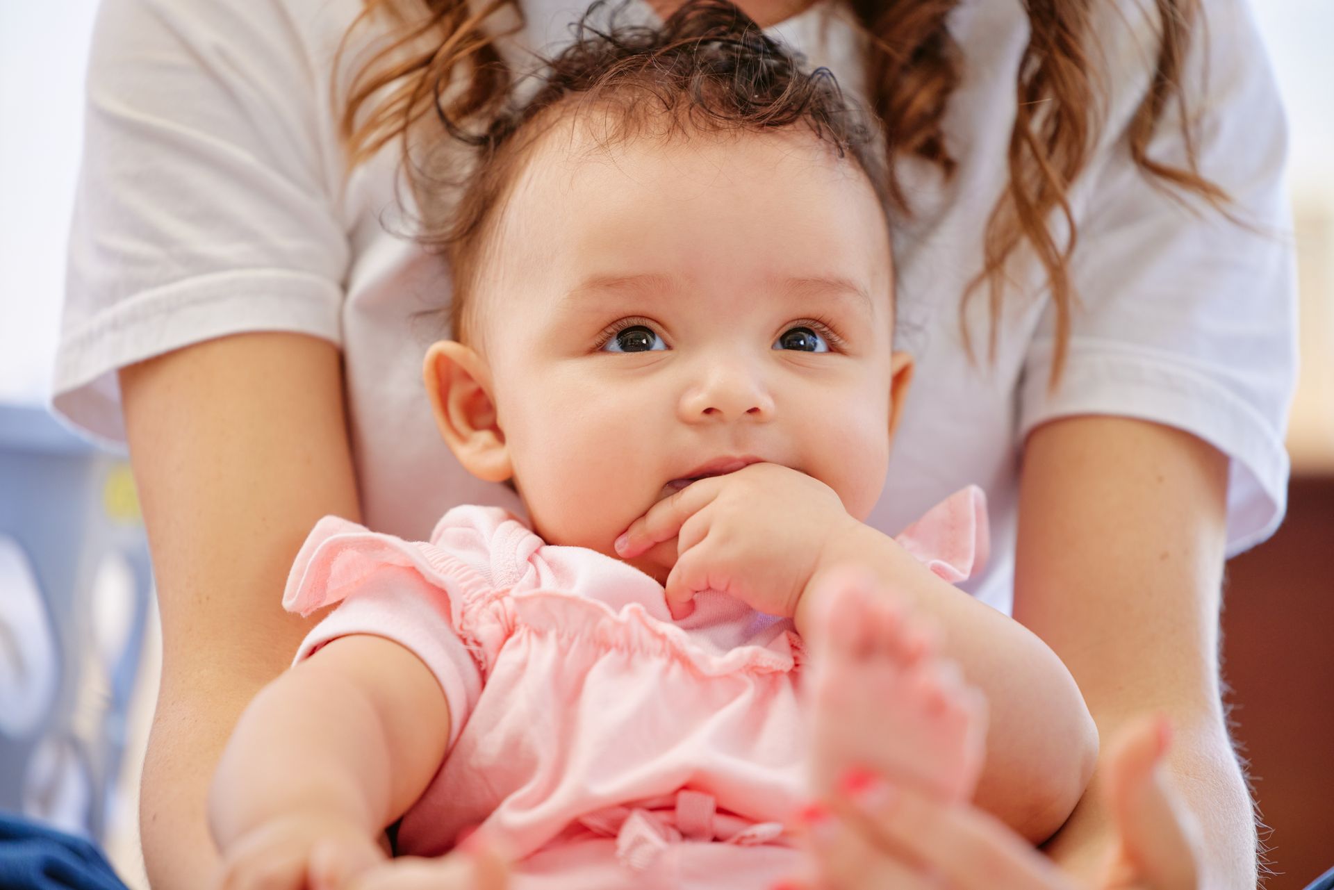 A woman is holding a baby in her arms in a pink dress.