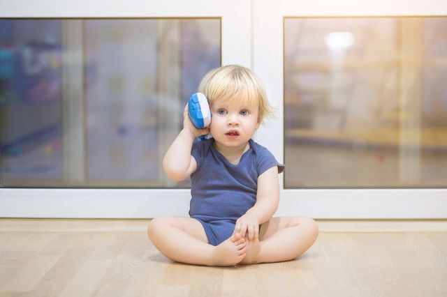 A baby is sitting on the floor talking on a toy phone.