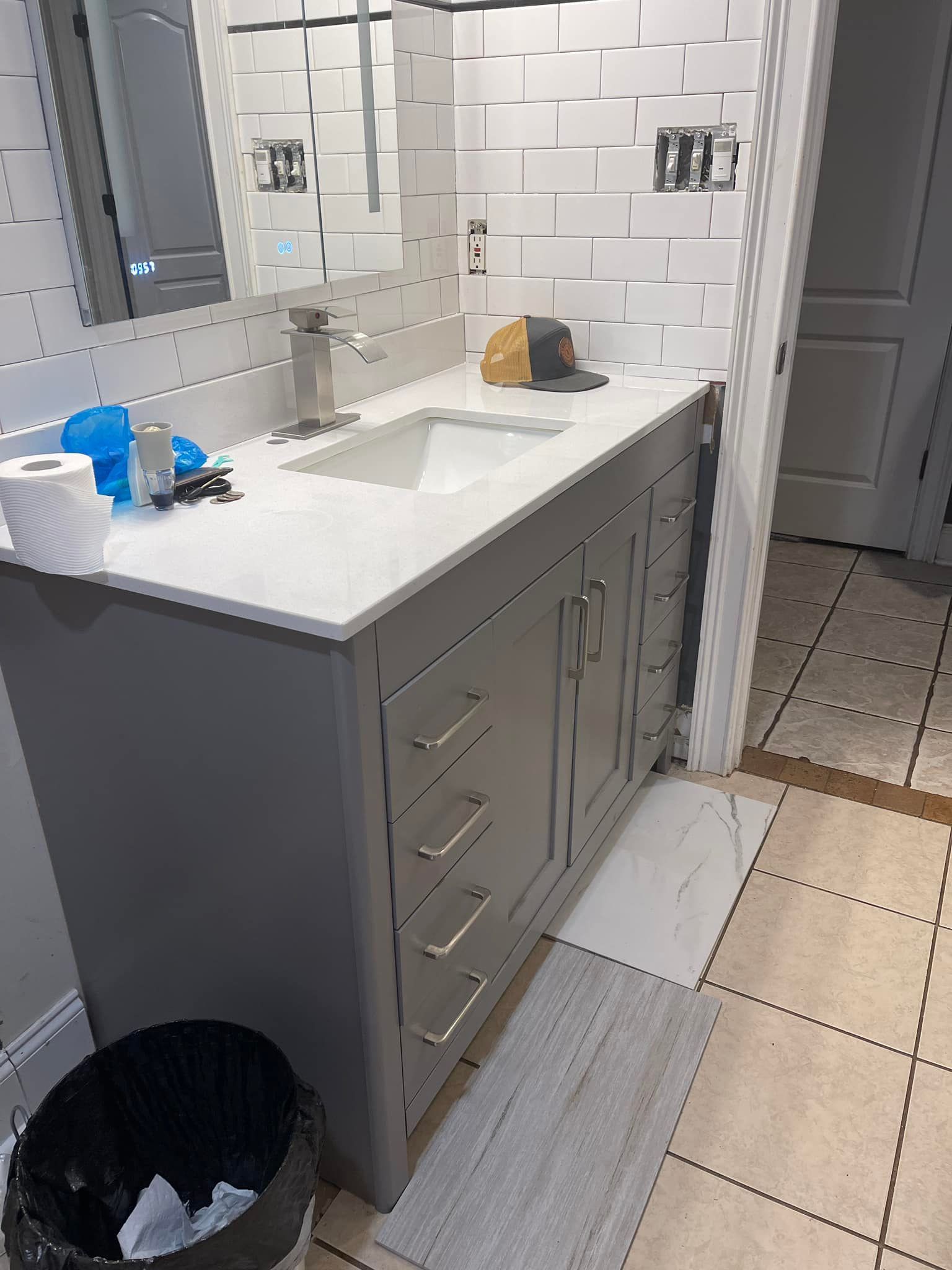 A bathroom with a sink , mirror and trash can.