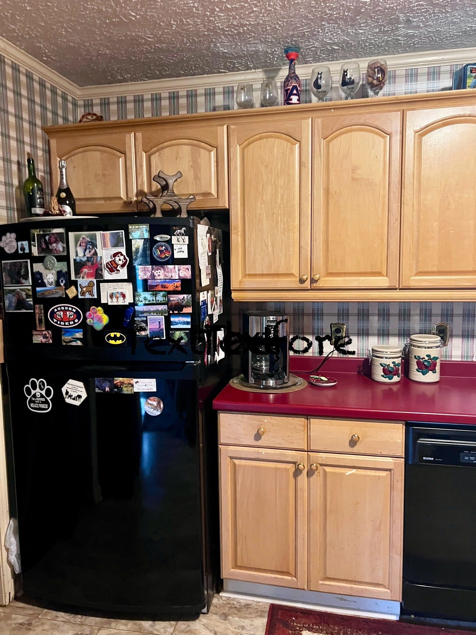 Black refrigerator next to light wood cabinets and red counter; kitchen.