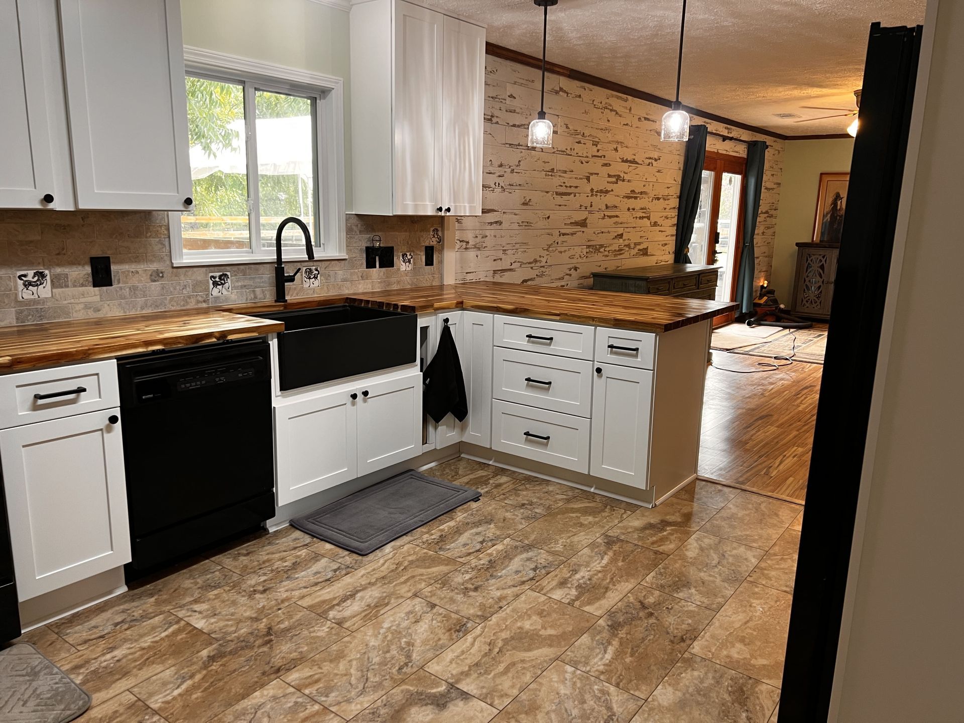 White kitchen with black appliances, wooden countertops, and a stone wall.