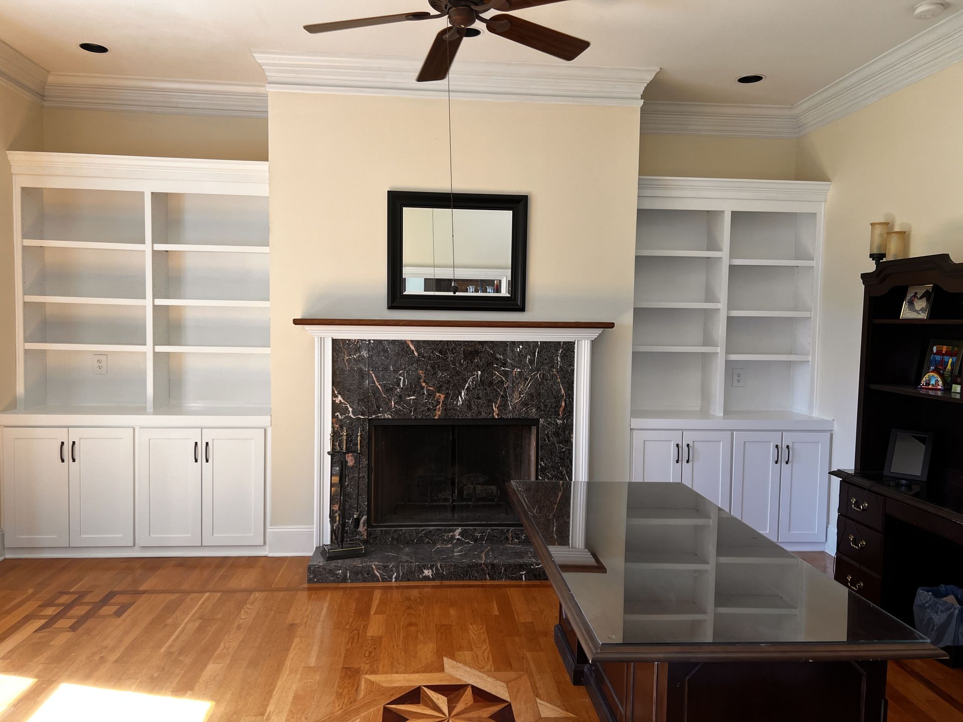 Built-in white bookshelves flank a fireplace with a black marble surround and mirror. Wooden floors.