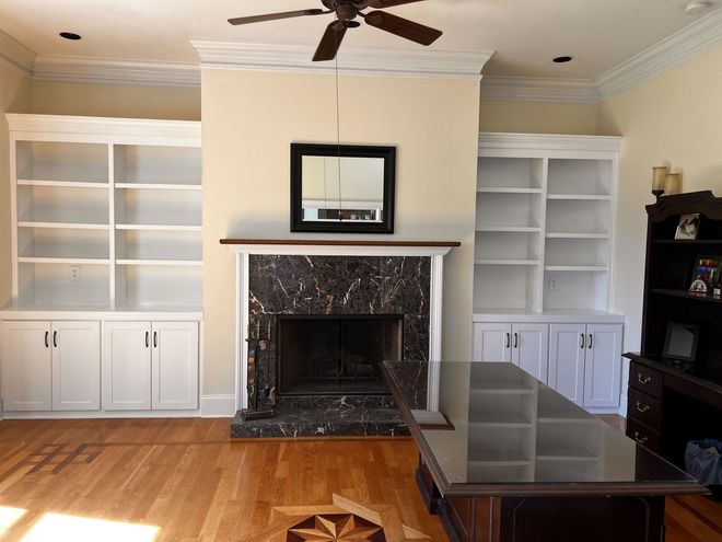 Living room with fireplace, built-in white bookshelves, hardwood floors, and a dark rectangular mirror.