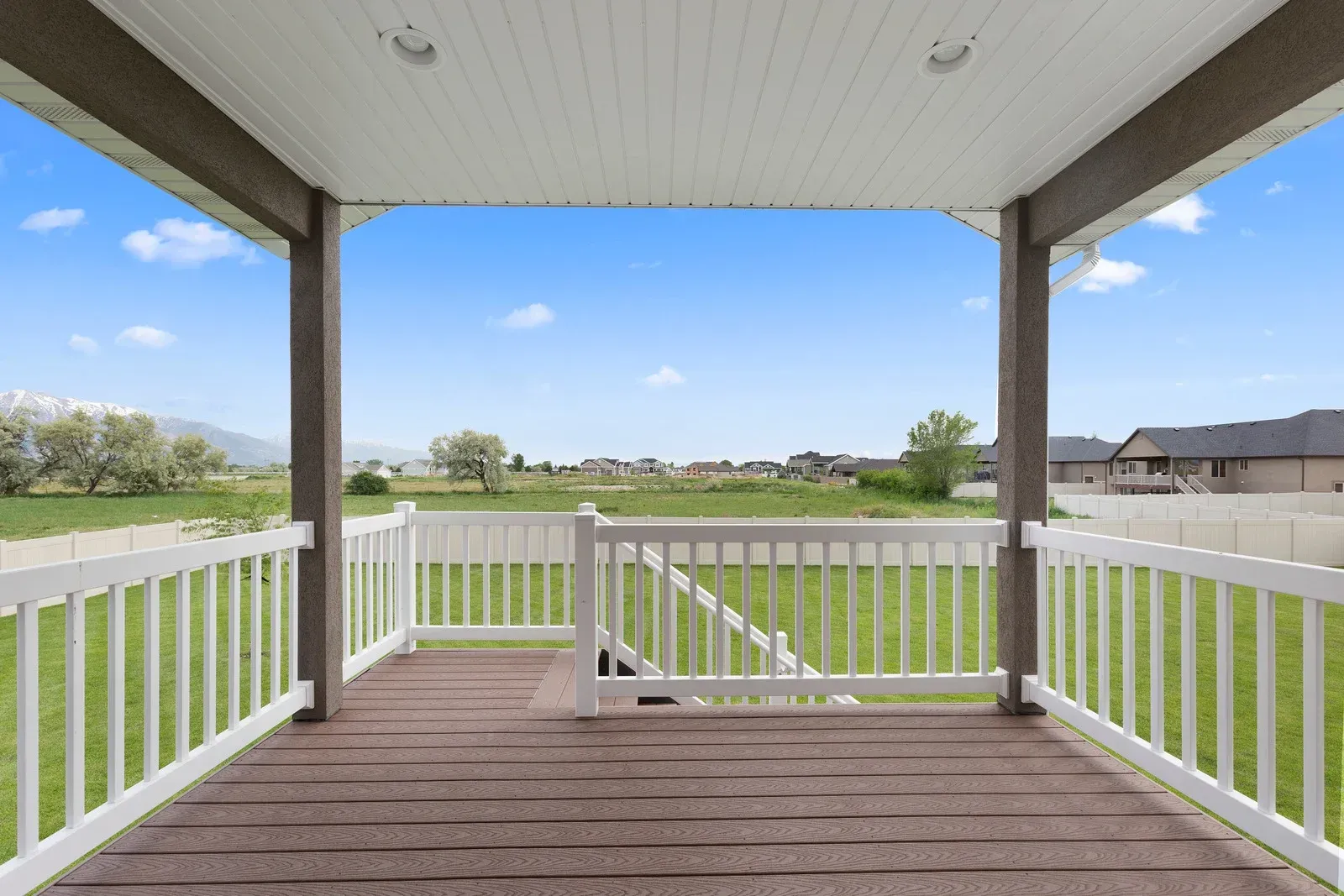 An empty porch with a white railing and a view of a field.