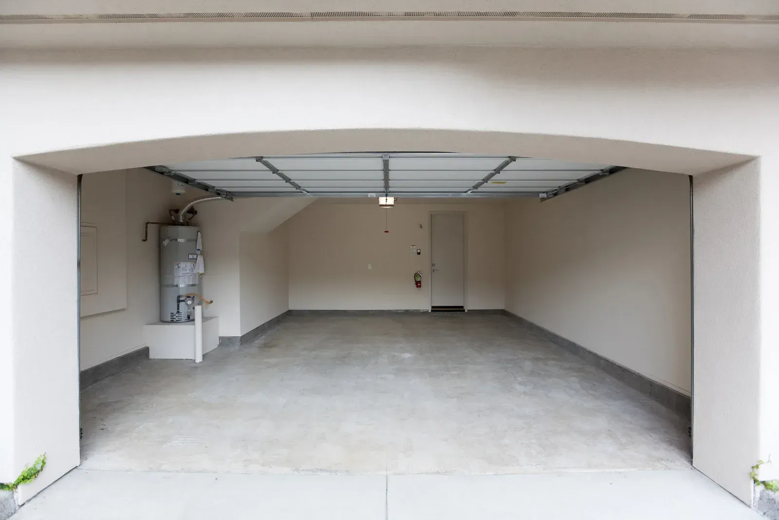 An empty garage with a door open and a water heater.