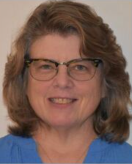 A woman wearing glasses and a blue shirt is smiling for the camera.